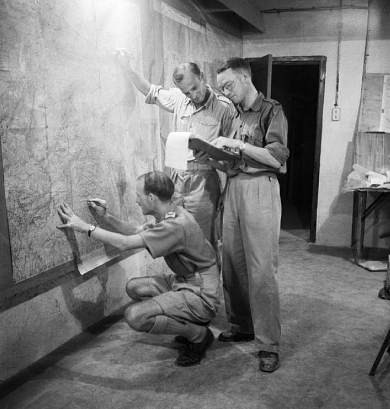 Staff officers plotting troop positions during the invasion of Sicily on a wall map in the underground operations room at Malta. 